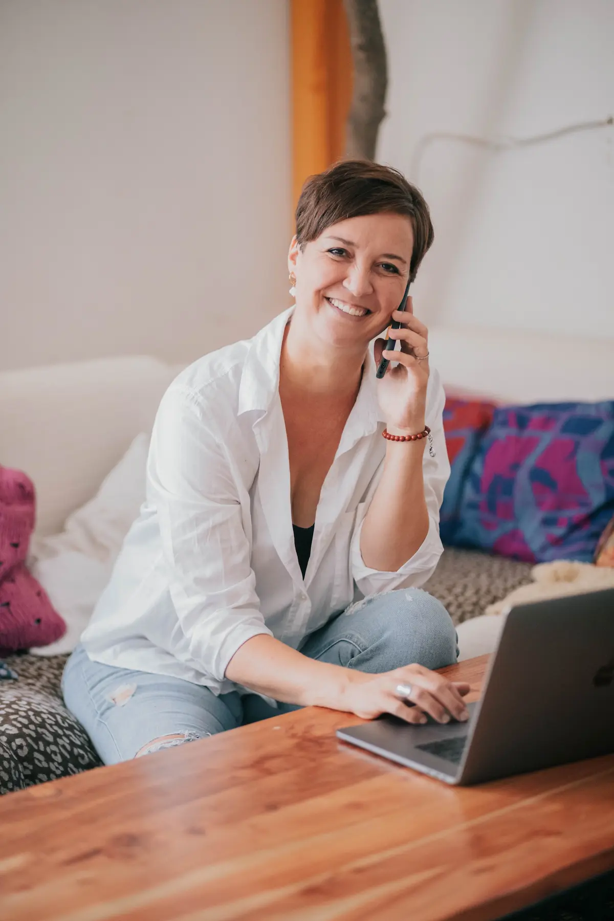 steffi sitzt auf einer couch, telefoniert und tippt auf ihrem laptop, während sie in die kamera lächelt